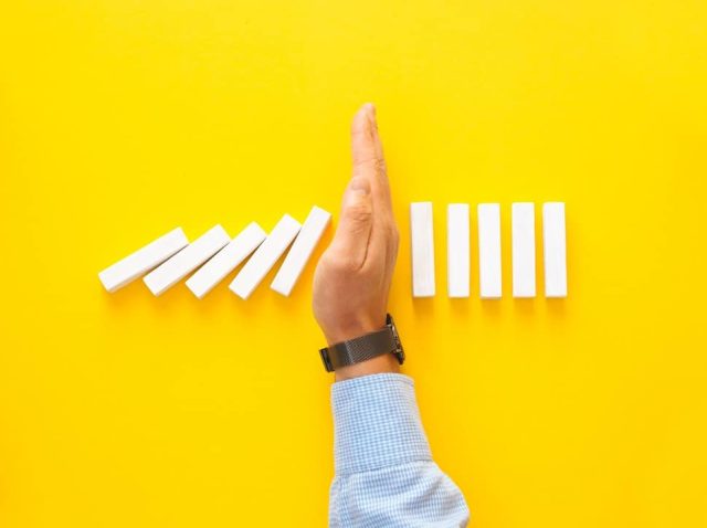 businessman-hand-stopping-falling-dominos-on-yello-RZ4GZ39