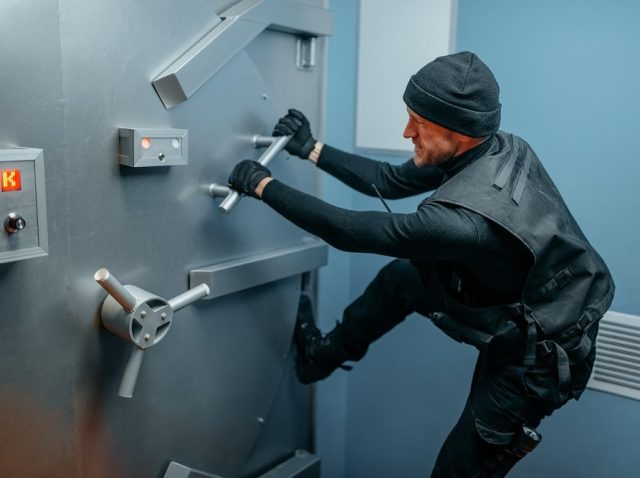 Robber in black uniform trying to break vault lock